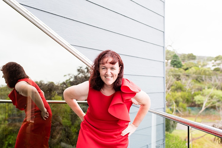 Suzanne Culberg in a red dress, hands on hips and leaning forward, laughing